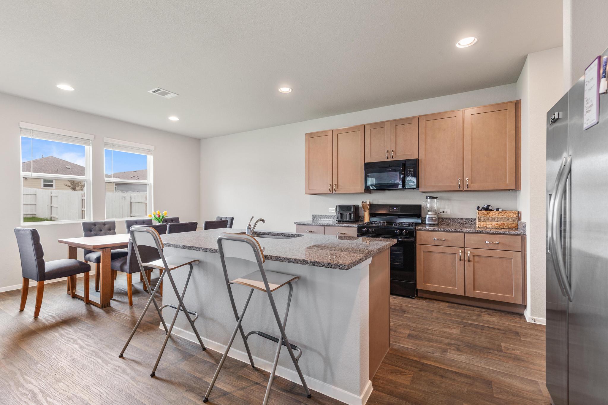 242 Barley Lane Elgin, TX 78621 - Photo 11 of 31 Open-concept kitchen featuring granite countertops, wood-finish flooring, recessed lighting, and a stainless steel refrigerator