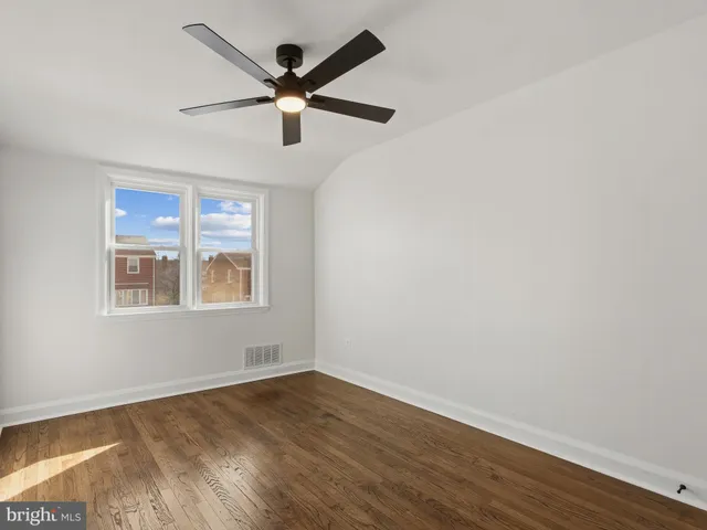 an empty room with wooden floor ceiling fan and windows