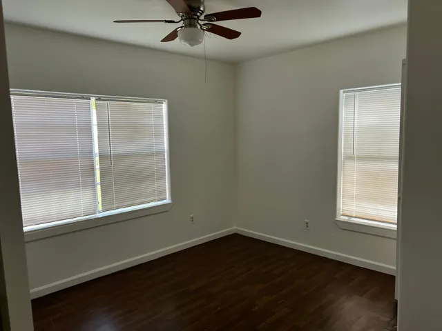 an empty room with wooden floor fan and windows