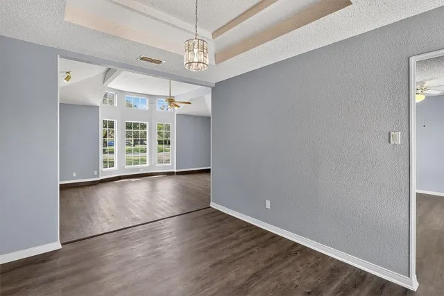 an empty room with wooden floor chandelier and windows