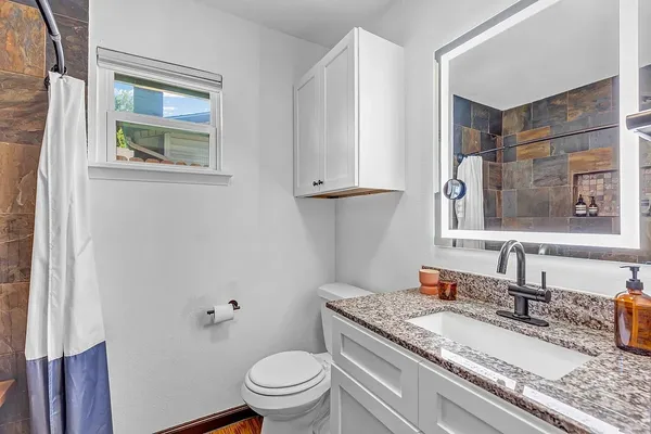 a bathroom with a granite countertop toilet a sink and a mirror