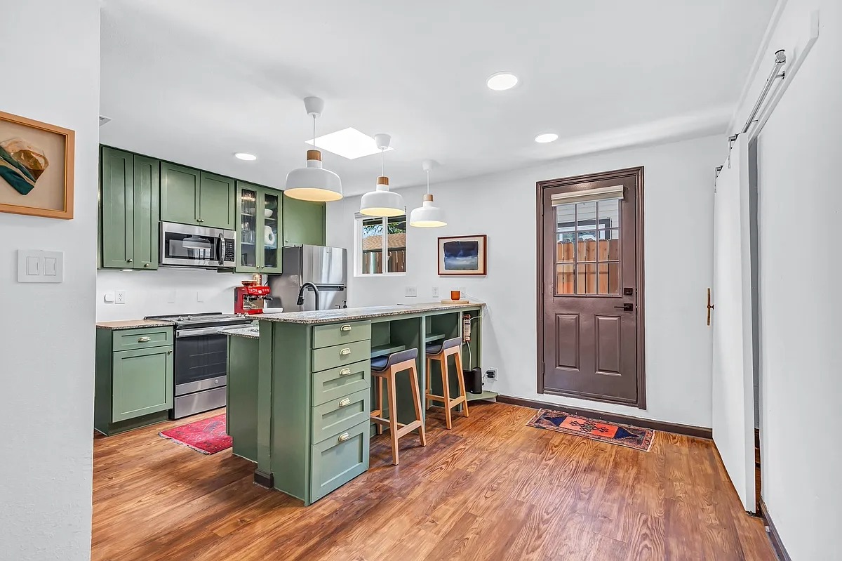 2307 Teri Road Austin, TX 78744 - Photo 6 of 28 Kitchen with green cabinets, glass insert cabinets, a kitchen bar, and stainless steel appliances