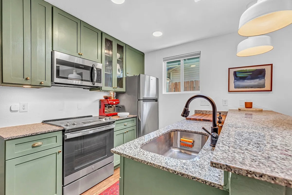2307 Teri Road Austin, TX 78744 - Photo 9 of 28 Kitchen with green cabinetry, light stone counters, stainless steel appliances, glass fronted cabinets, and light wood-style floors