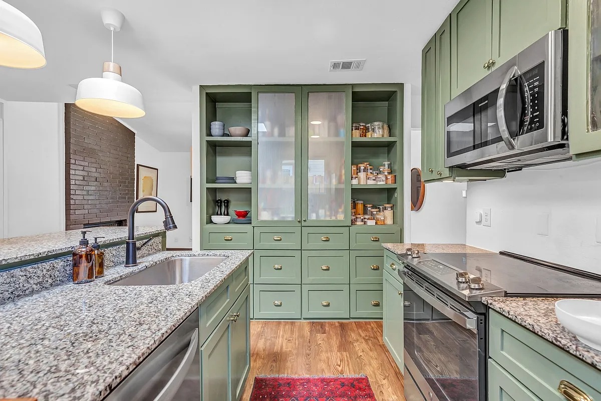 2307 Teri Road Austin, TX 78744 - Photo 10 of 28 Kitchen featuring green cabinetry, stainless steel appliances, glass insert cabinets, hanging light fixtures, and light stone countertops