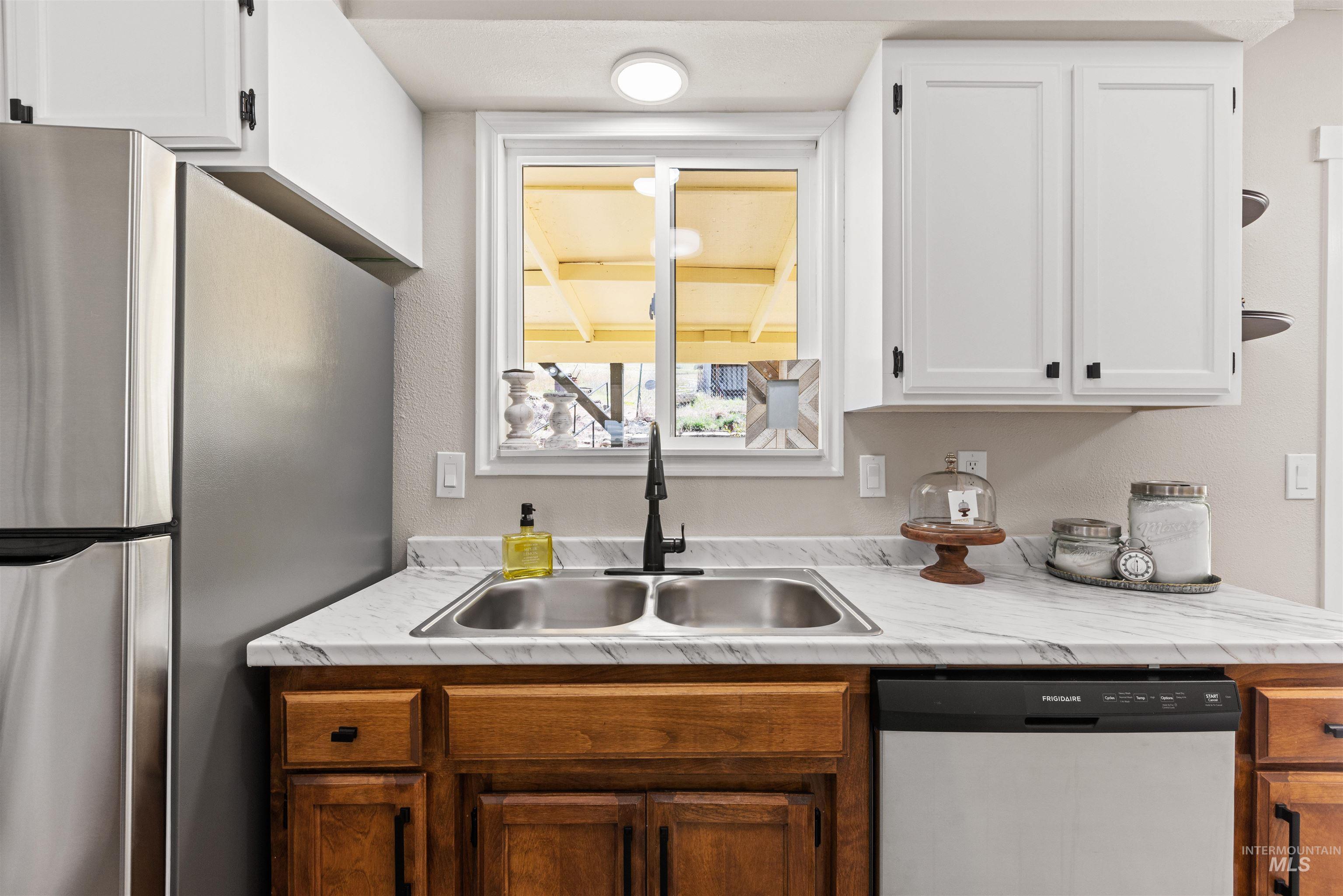 12184 Hill Road Payette, ID 83661 - Photo 15 of 35 Kitchen featuring a double basin stainless steel sink, black faucet, white upper cabinetry with black hardware, and wood-finish lower cabinetry