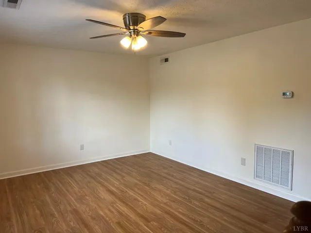 an empty room with wooden floor fan and windows