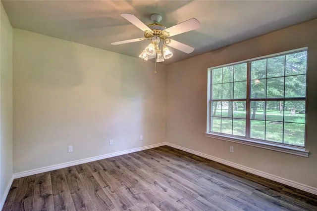 an empty room with wooden floor fan and windows