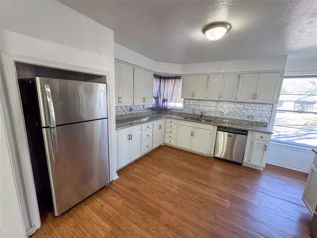 a kitchen with granite countertop a refrigerator a sink dishwasher a stove and white cabinets with wooden floor