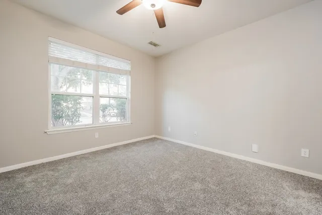 an empty room with chandelier fan and windows