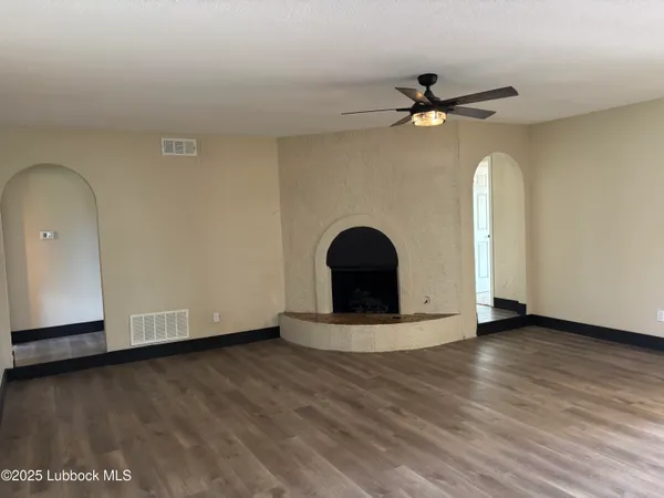 an empty room with wooden floor chandelier fan and windows