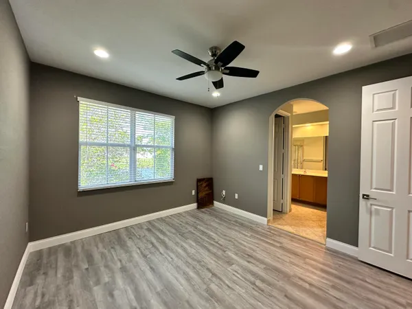 an empty room with wooden floor fan and windows