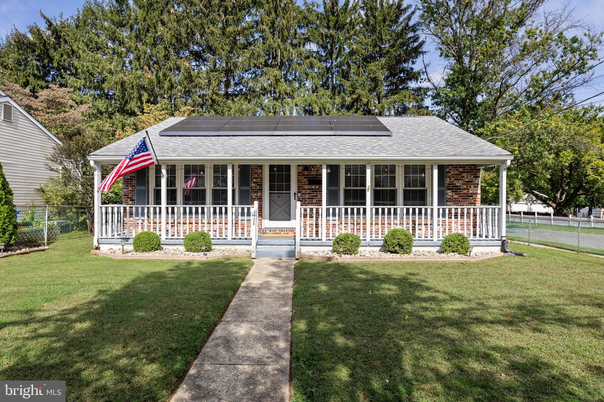 a view of house in front of a big yard with large trees and plants