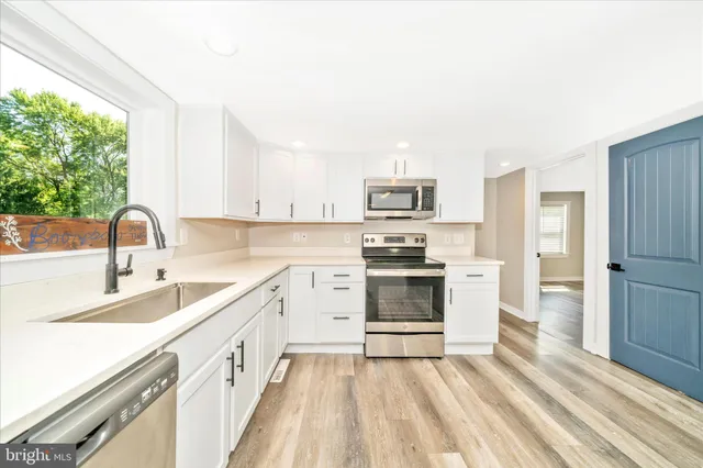 a kitchen with a sink a stove a refrigerator and white cabinets with wooden floor