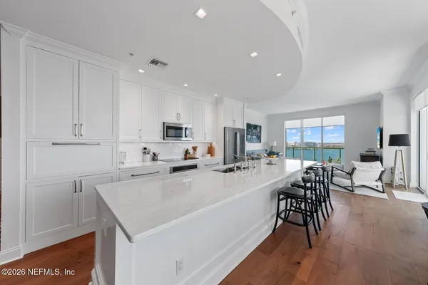 a kitchen with stainless steel appliances a refrigerator a stove a sink a dining table and chairs with wooden floor