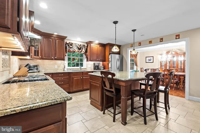 a kitchen with stainless steel appliances granite countertop wooden cabinets a stove top oven a sink with dining table and chairs