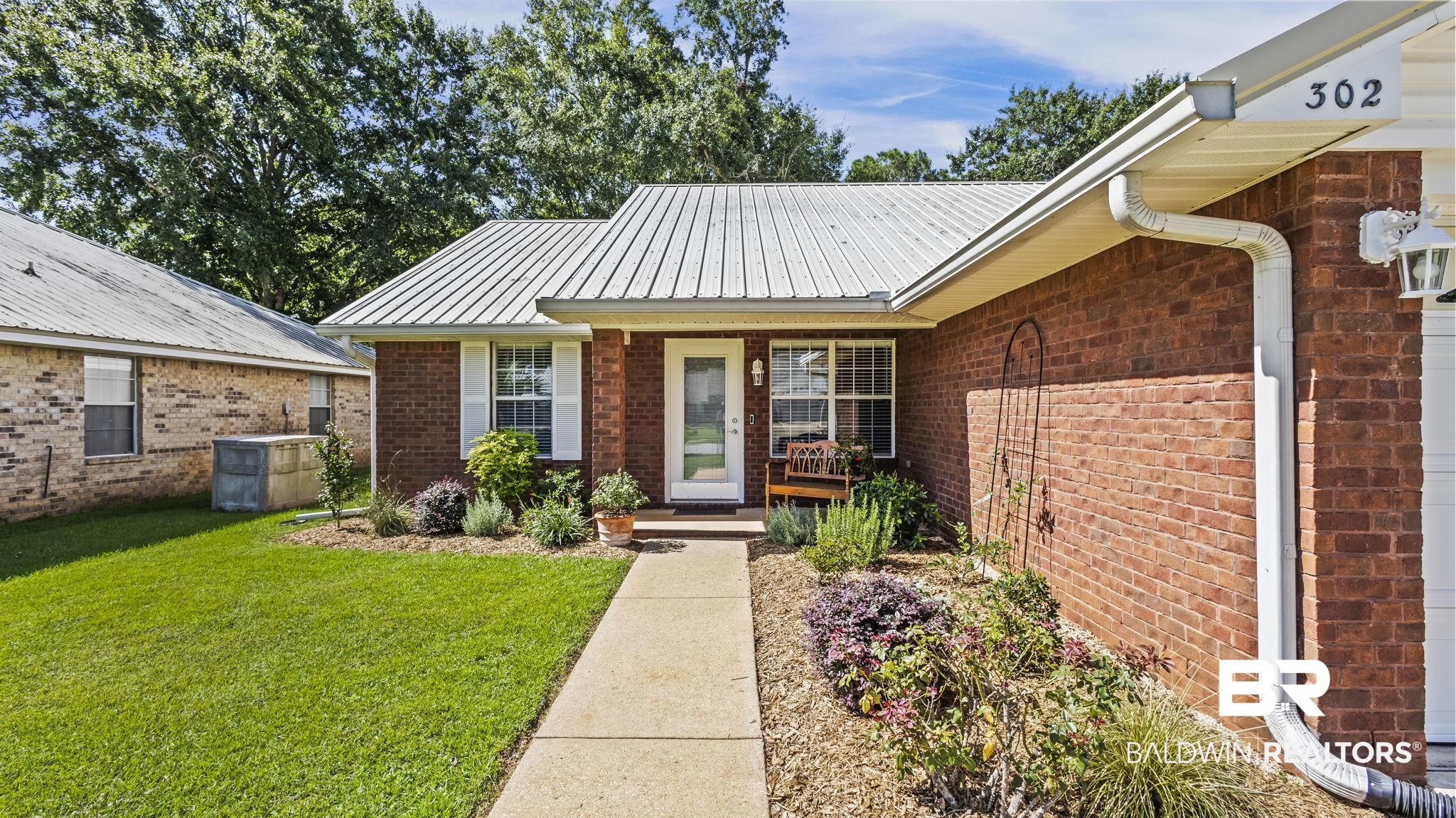 302 Cluster Street Foley, AL 36535 - Photo 5 of 28 View of exterior entry featuring a yard, brick siding, and a metal roof