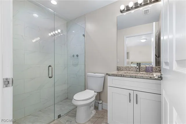 a bathroom with a granite countertop shower a toilet a sink and a mirror