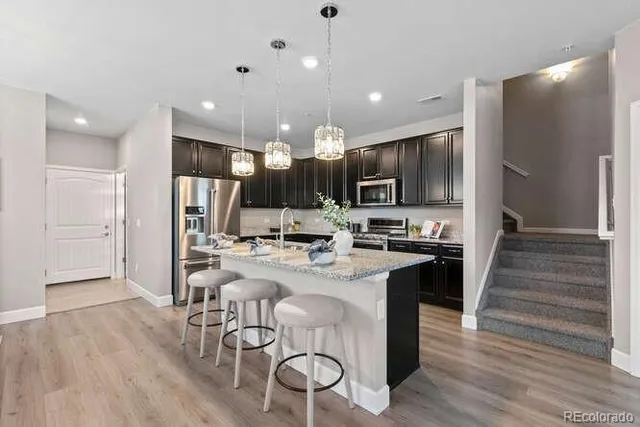 a kitchen with stainless steel appliances kitchen island granite countertop a stove top oven a refrigerator a sink and white cabinets with wooden floor