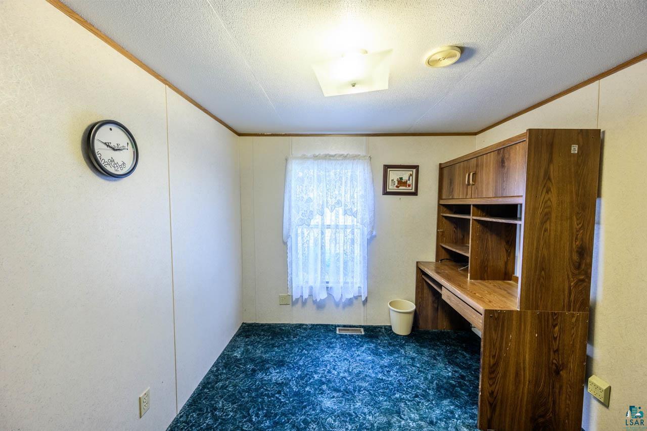 705 4th Street North Biwabik, MN 55708 - Photo 9 of 29 Room featuring a built-in wood-finish desk with upper cabinetry and shelving, patterned green carpeting, and neutral-toned walls