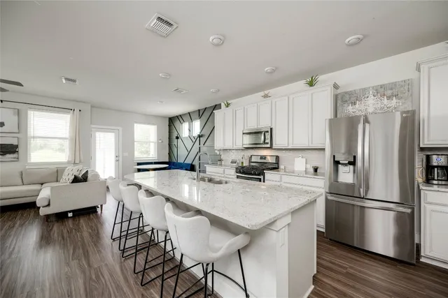 a kitchen with stainless steel appliances a refrigerator a stove a sink dishwasher and white cabinets with wooden floor