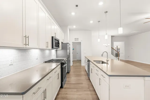 a view of a kitchen with kitchen island a large counter top space a sink stainless steel appliances and cabinets