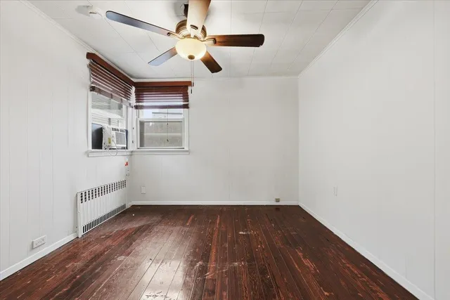 an empty room with wooden floor chandelier fan and windows