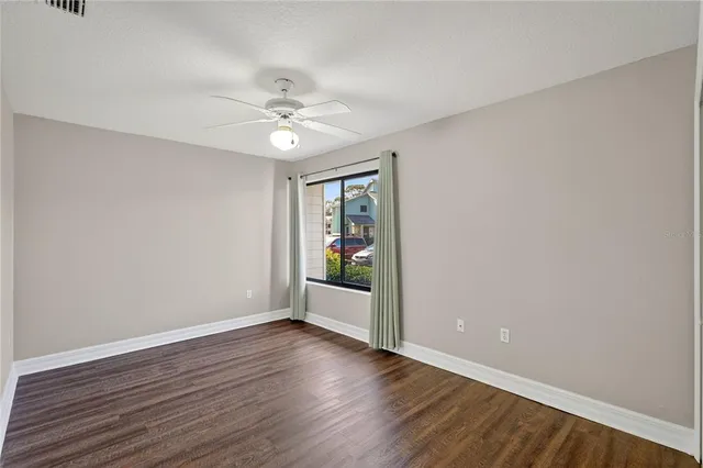 an empty room with wooden floor chandelier fan and windows