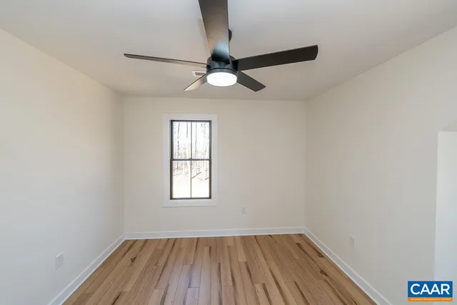 an empty room with wooden floor ceiling fan and windows