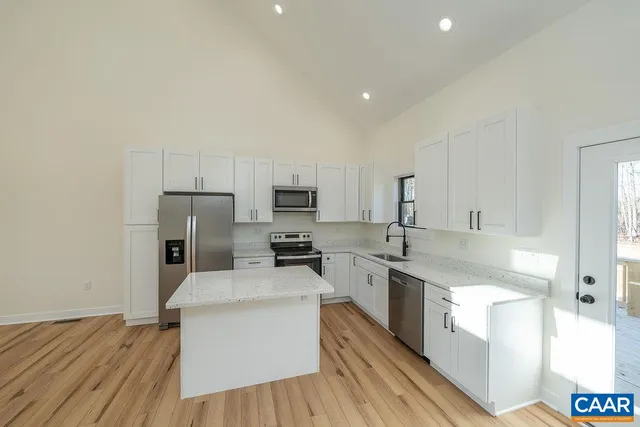 a kitchen with stainless steel appliances a sink a stove a refrigerator cabinets and a wooden floor