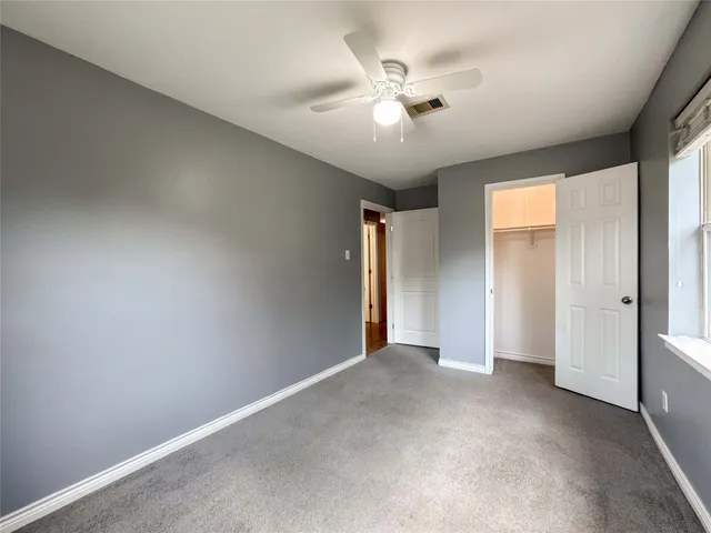 an empty room with chandelier fan and windows