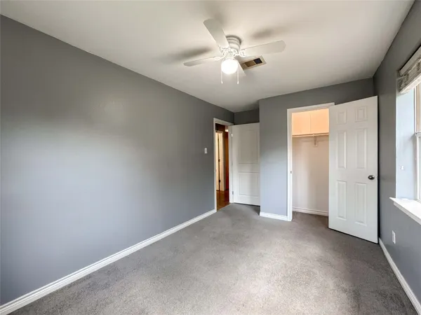 an empty room with chandelier fan and windows