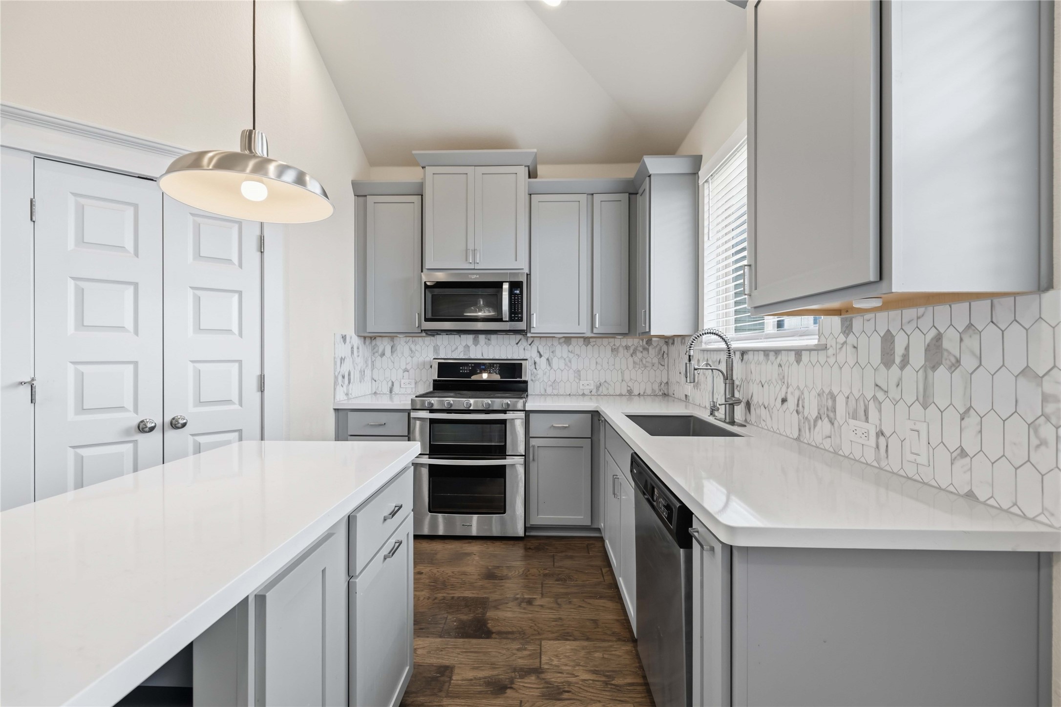 1722 Rowdy Loop, Unit 7 Leander, TX 78641 - Photo 11 of 37 Elegant kitchen featuring sleek gray cabinetry, stainless steel appliances, and a stylish hexagonal tile backsplash. The quartz countertops and modern pendant lighting enhance the contemporary design.