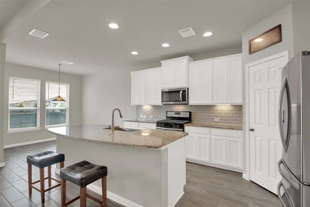 a kitchen with stainless steel appliances granite countertop a sink a stove a refrigerator cabinets and a dining table with wooden floor