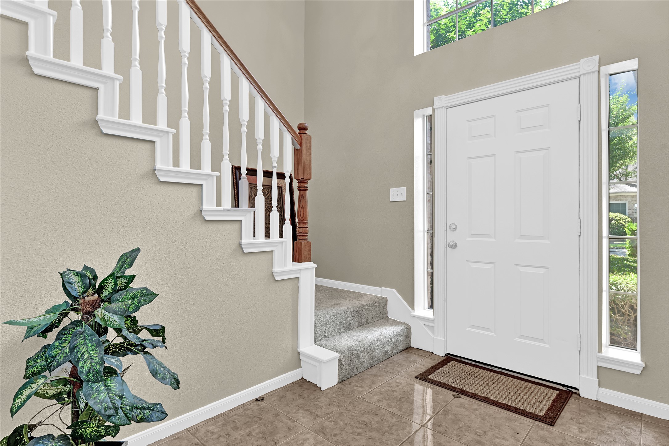 14420 Walters Road, Unit 16 Houston, TX 77014 - Photo 3 of 27 Bright and welcoming entryway featuring a white front door with side windows, tiled floor, a carpeted staircase with white railings, and a decorative plant.