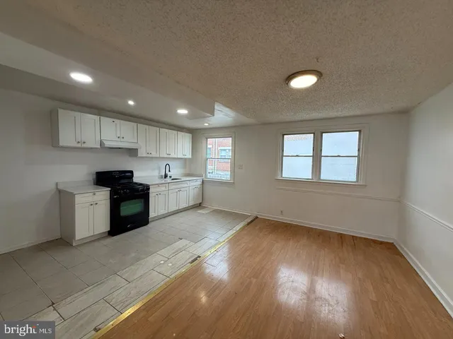 a large kitchen with stainless steel appliances granite countertop a stove a sink a refrigerator white cabinets and wooden floor