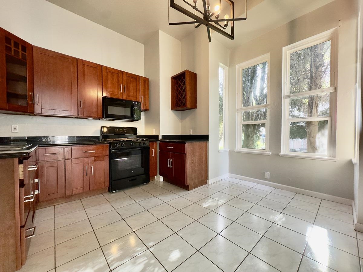 1022 Chestnut Street Oakland, CA 94607 - Photo 45 of 60 Kitchen with black appliances, light tile patterned floors, a chandelier, glass insert cabinets, and dark stone countertops