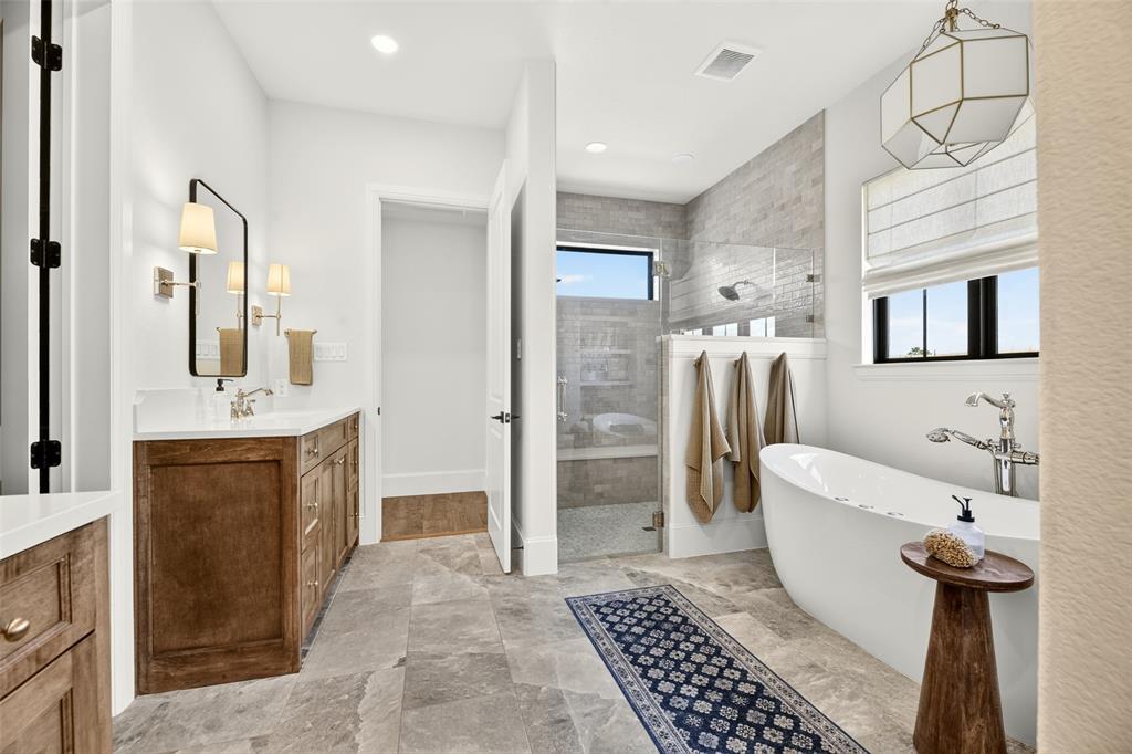 10932 Gregory Road Sanger, TX 76266 - Photo 23 of 40 Freestanding soaking tub, walk-in shower with glass enclosure, wood-finish vanity with countertop, wall-mounted light fixtures, and large format tile flooring