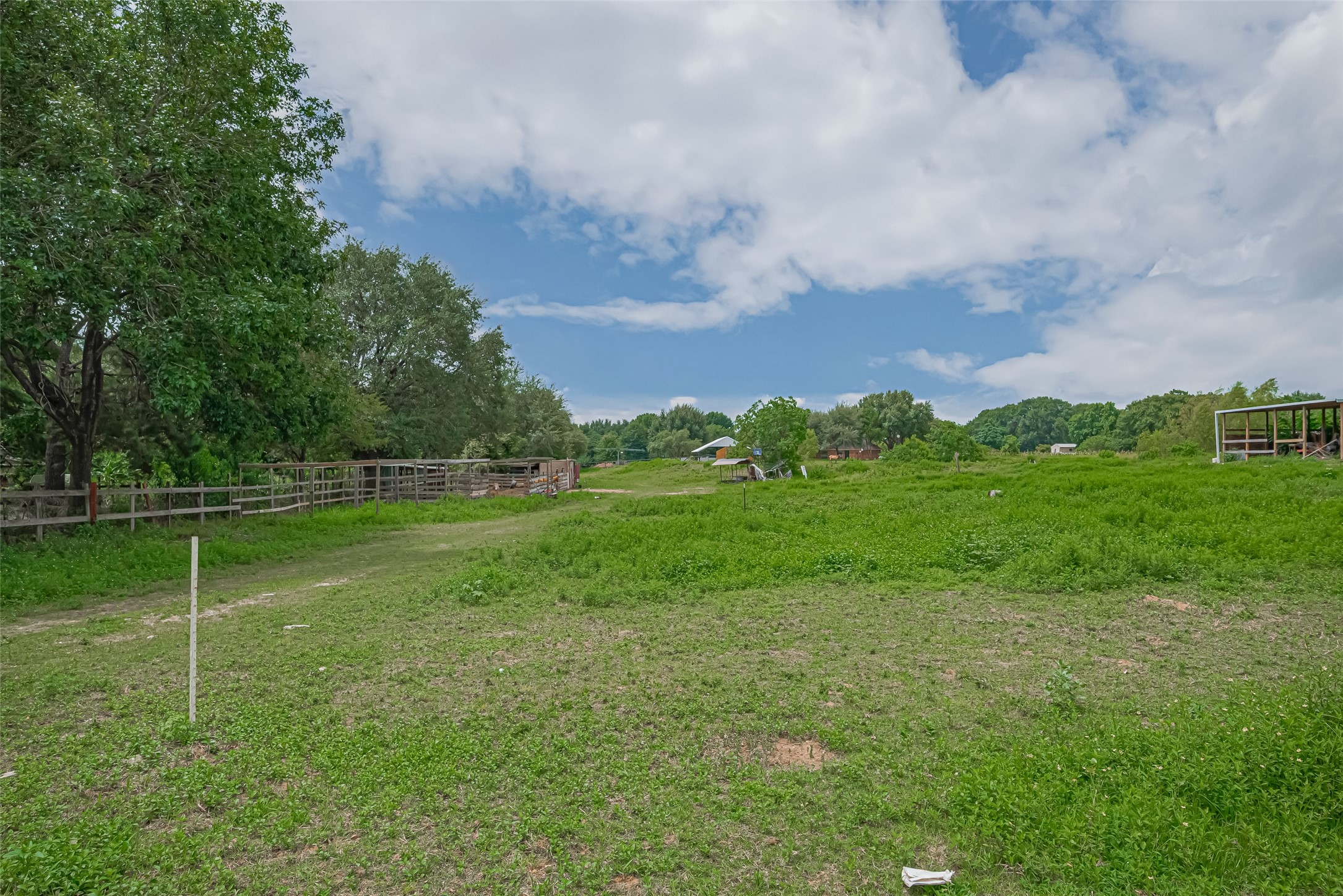 35535 Windmill Road Hempstead, TX 77445 - Photo 18 of 41 Expansive green land with scattered trees, a wooden fence, and a partly cloudy sky, offering a serene rural setting ideal for building or farming.