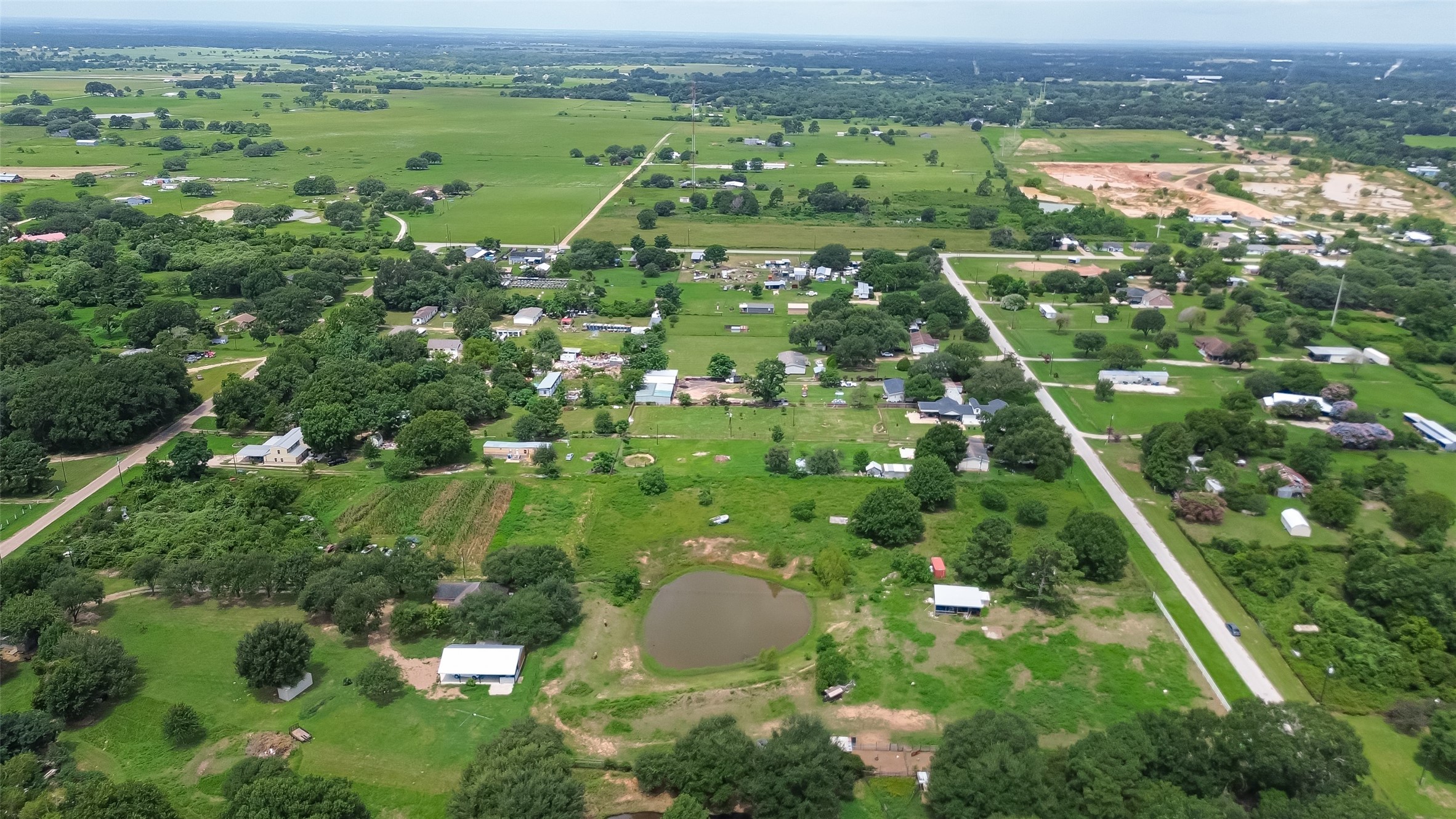 35535 Windmill Road Hempstead, TX 77445 - Photo 28 of 41 This aerial photo shows a spacious rural area with scattered homes, lush greenery, and a small pond. The landscape is open and dotted with trees, providing a serene and expansive countryside view. Ideal for those seeking a peaceful, rural lifestyle.