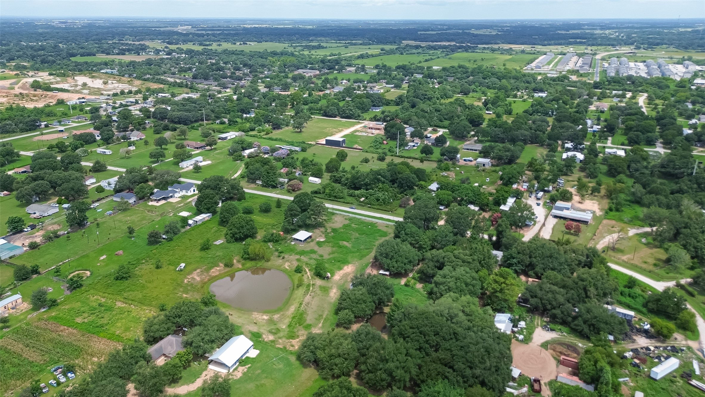 35535 Windmill Road Hempstead, TX 77445 - Photo 29 of 41 This aerial photo showcases a spacious rural area with lush greenery, scattered homes, and open fields. A small pond and winding roads enhance the scenic landscape, offering a tranquil, country-living environment. Ideal for those seeking space and nature.