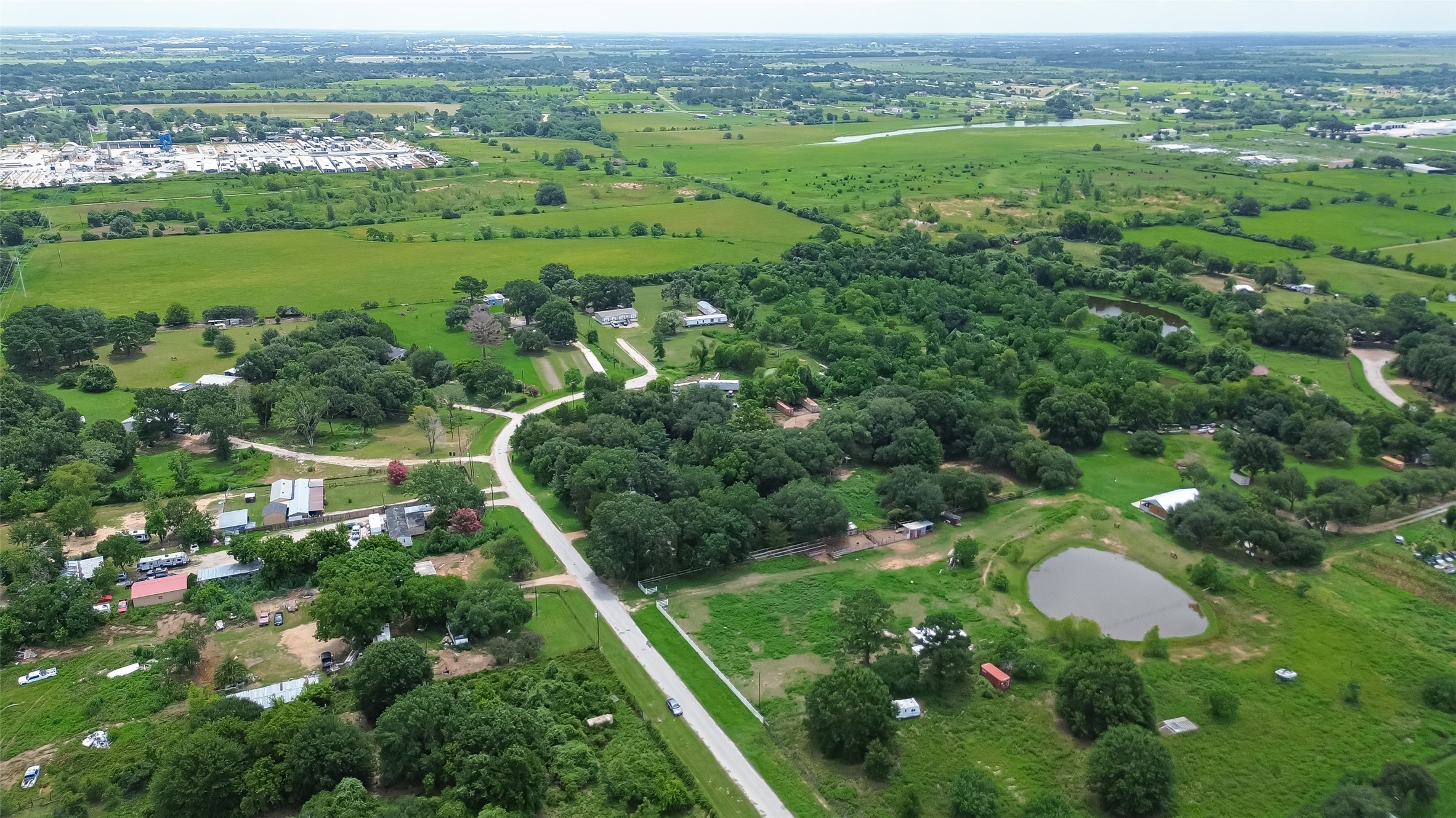 35535 Windmill Road Hempstead, TX 77445 - Photo 34 of 41 This aerial photo showcases a serene rural setting with lush greenery, scattered homes, winding roads, and a small pond, offering a peaceful countryside living environment.