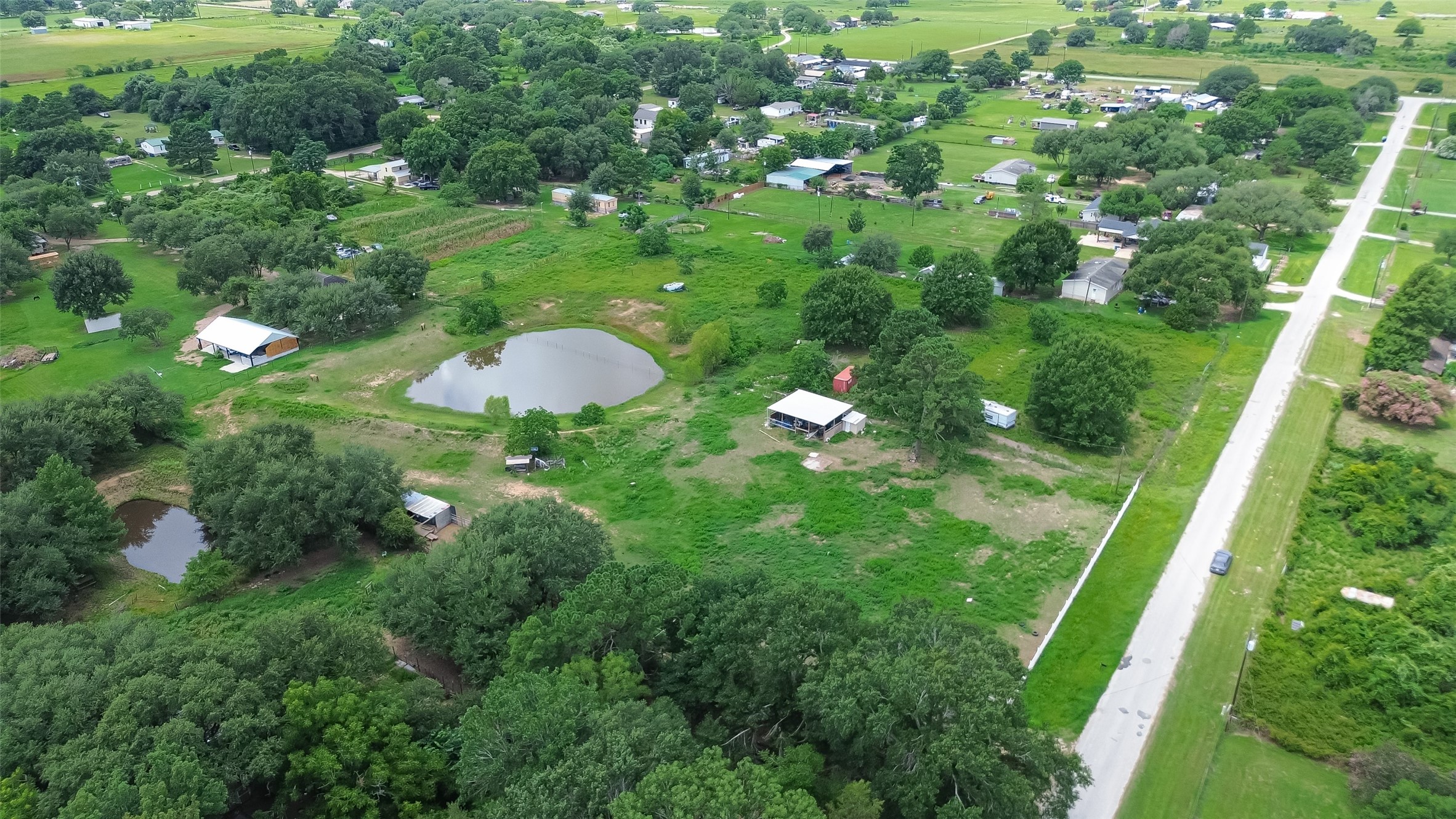 35535 Windmill Road Hempstead, TX 77445 - Photo 40 of 41 This aerial photo showcases a spacious, green rural area with scattered homes, small ponds, and a few outbuildings. It's a peaceful setting with ample greenery and open space, ideal for those seeking tranquility and a connection with nature.