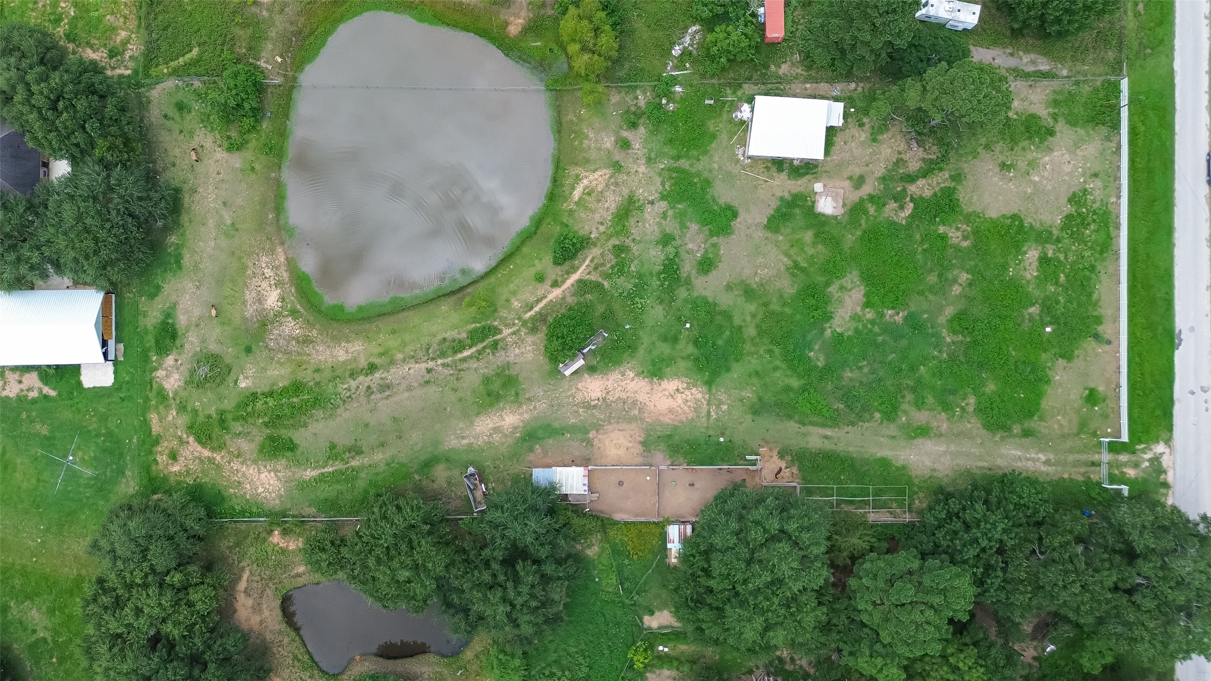 35535 Windmill Road Hempstead, TX 77445 - Photo 41 of 41 This aerial photo shows a large property with two ponds, open green spaces, and a few structures, including a barn. The land is bordered by trees and a road on one side, offering a peaceful, rural setting.