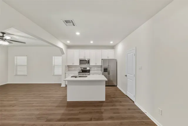 a large white kitchen with kitchen island a stove a sink a refrigerator and white cabinets with wooden floor