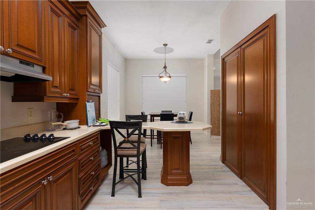 210 North 18th Street Hidalgo, TX 78557 - Photo 6 of 24 Kitchen with brown cabinetry, pendant lighting, black electric stovetop, under cabinet range hood, and a breakfast bar area