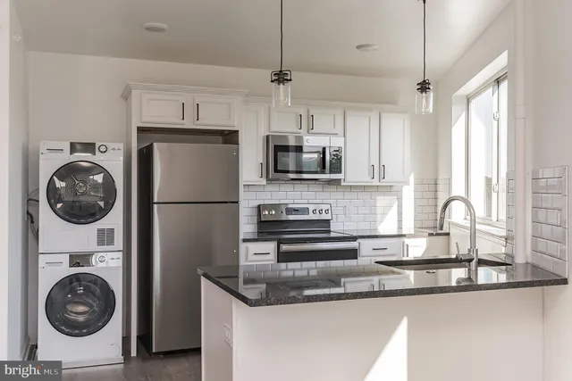 a kitchen with stainless steel appliances granite countertop a sink a stove a washer and dryer