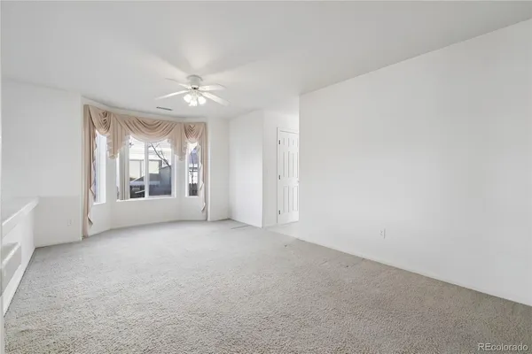 an empty room with chandelier fan and windows