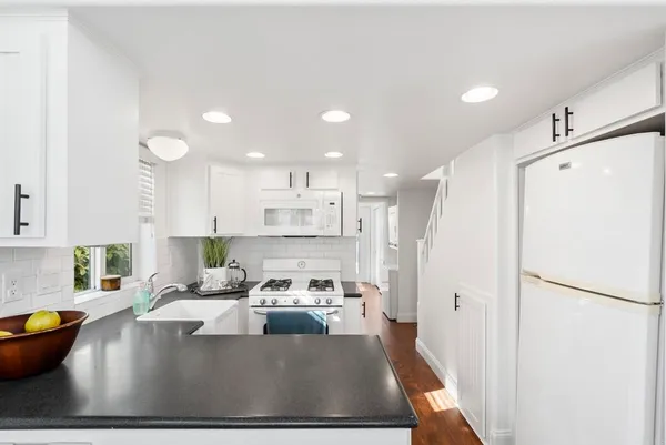 a large white kitchen with stainless steel appliances granite countertop a refrigerator a sink a stove and a refrigerator with wooden floor