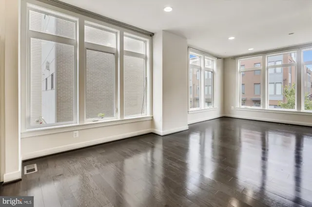 an empty room with wooden floor and windows with curtains
