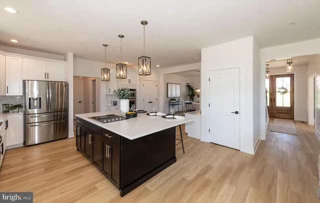 a kitchen with stainless steel appliances kitchen island a stove a sink a refrigerator and white cabinets with wooden floor